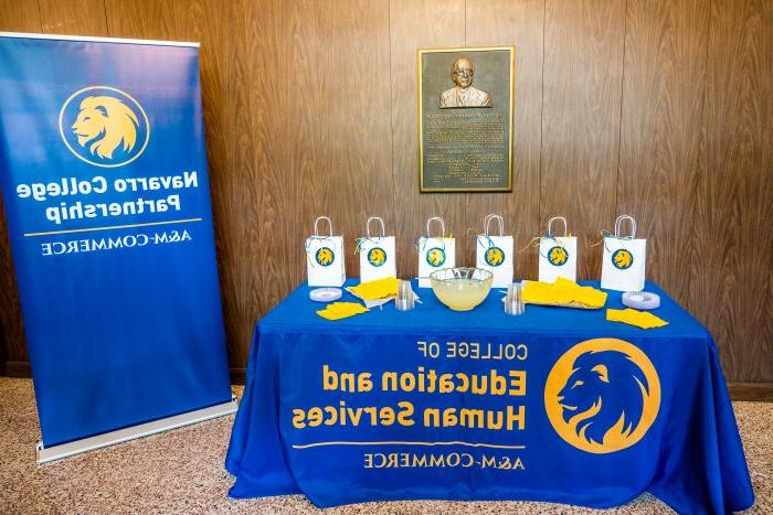 糖果袋和点心放在一张桌子上，桌子上装饰着蓝色和金色的桌布，旁边是一个a&移动商务 Navarro College Partnership flag banner.